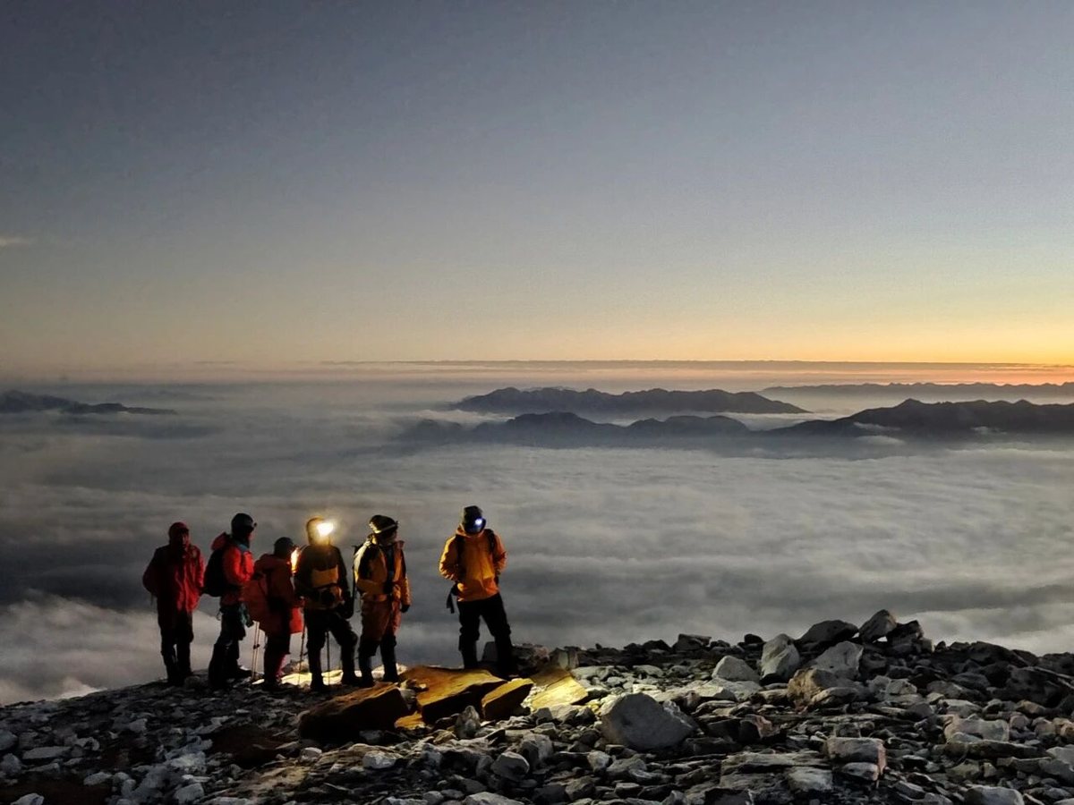 Hikers on a rocky ridge above a sea of cloud at sunrise